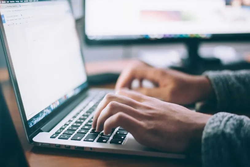 Hands typing on laptop keyboard in blurred office workspace environment